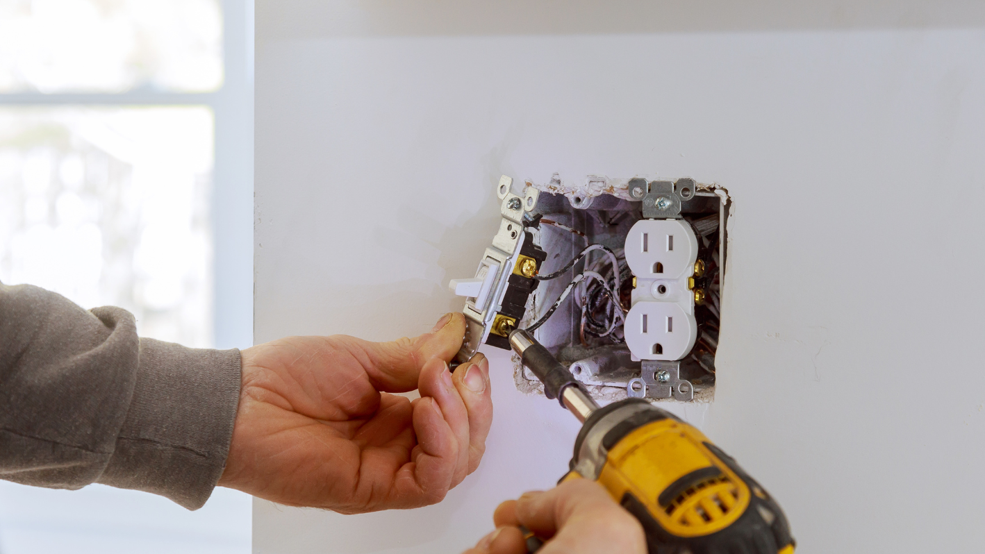 A person using a screwdriver to fix a light switch